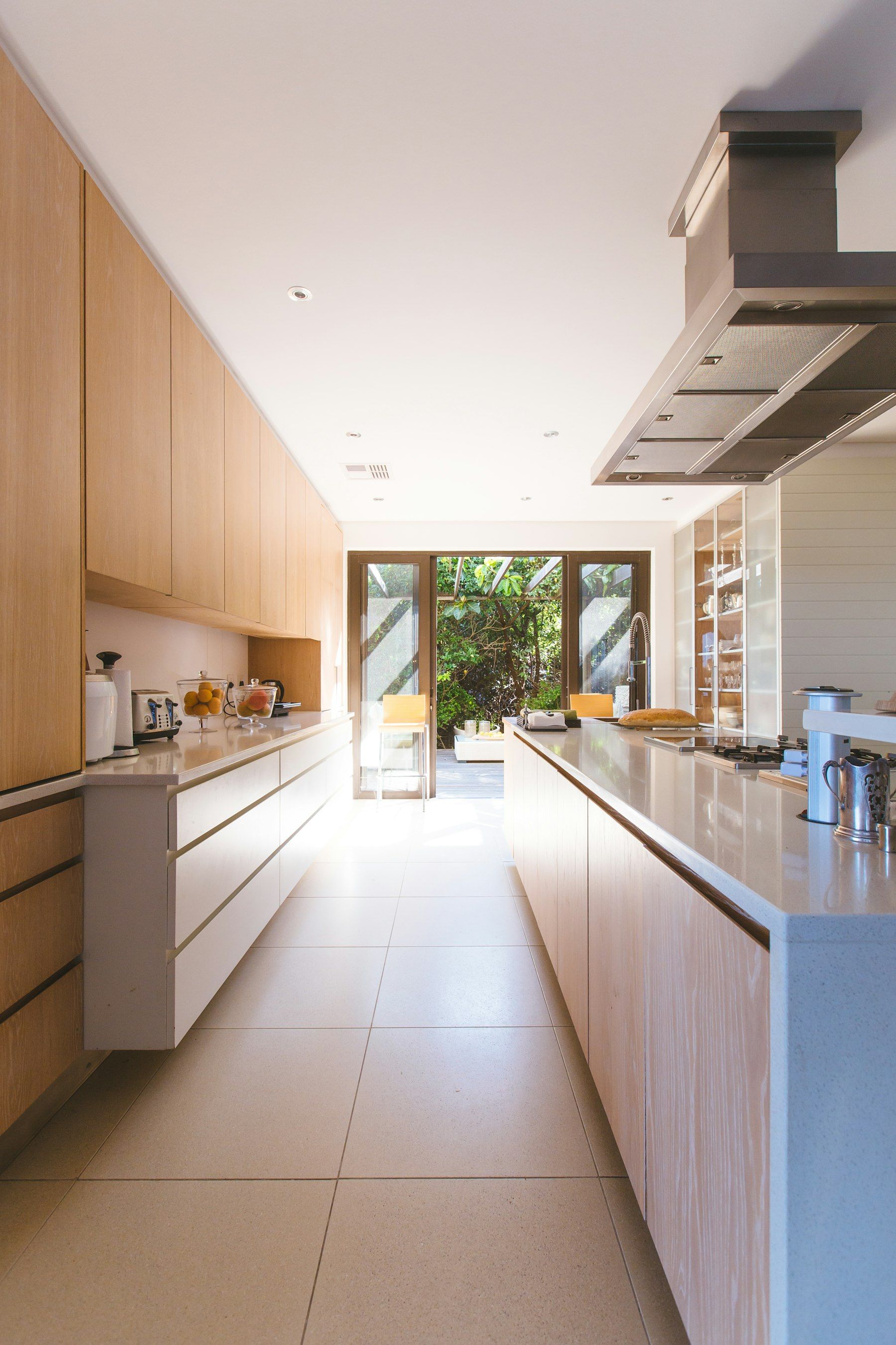 Galley kitchen with light oak cabinets, a long quartz island and glass doors to the garden